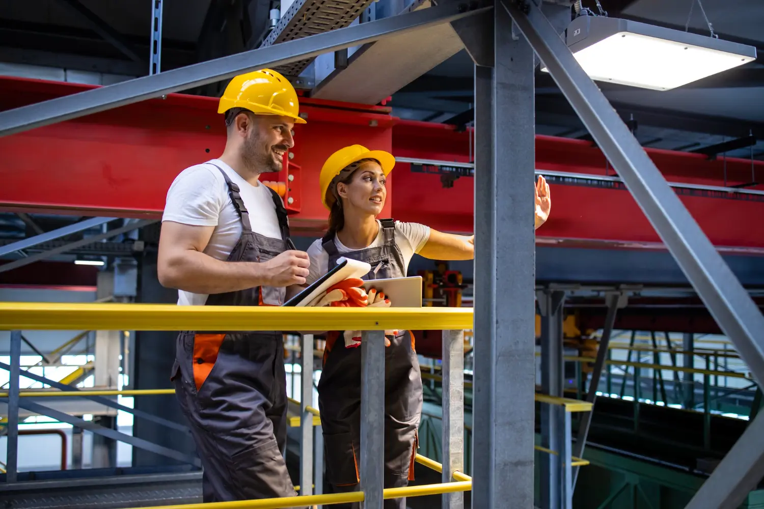 Two Canberra tradies in hard hats reviewing plans on an industrial walkway